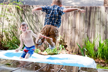two boys playing on inflatable pool outside during daytime thumbnail