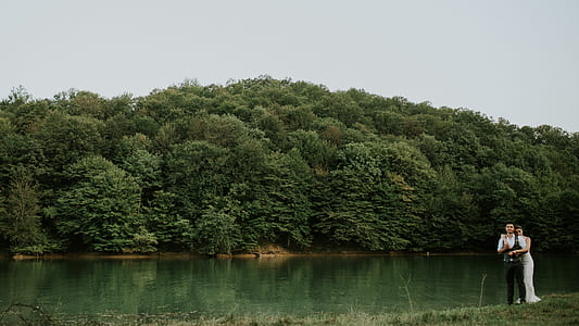 woman hugging man on grass field beside body of water during daytime thumbnail