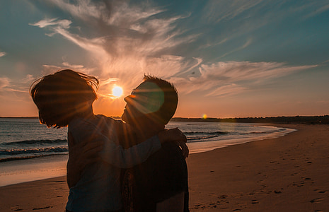 man carrying girl wearing white long-sleeved shirt walking on seashore during sunset thumbnail