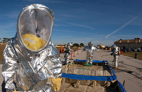 four people wearing aluminum suits while spraying on tacker blacktop road thumbnail
