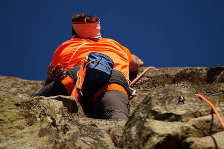 Person in Orange Shirt Climbing Rock during Daytime thumbnail