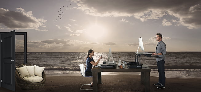 man and woman facing computer monitors on top of beach thumbnail