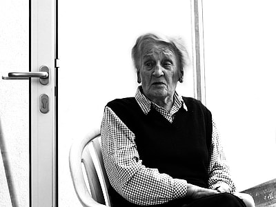 grayscale photo of man sitting on armchair beside door thumbnail