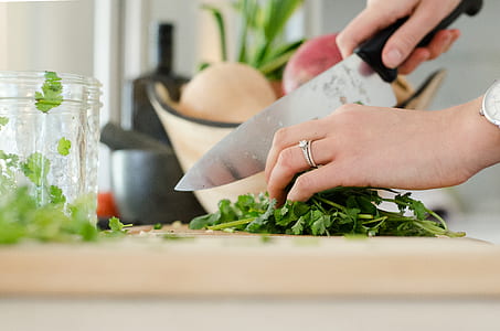 person chopping parsley on brown wooden board near clear glass jar thumbnail