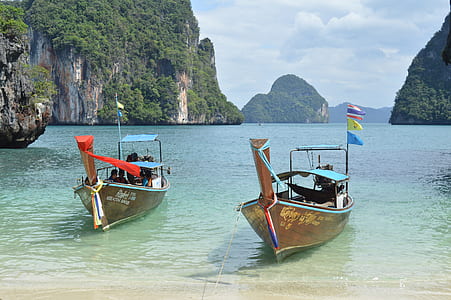 two brown boat on water near mountain thumbnail