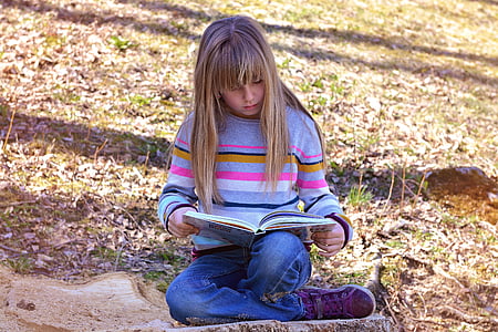girl reading book sitting on green grass at daytime thumbnail