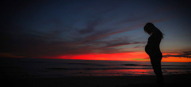 silhouette of pregnant women standing near sea during sunset thumbnail