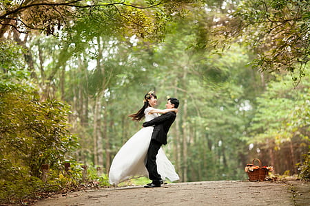 selective focus photo of a groom carrying bride under green tall trees thumbnail