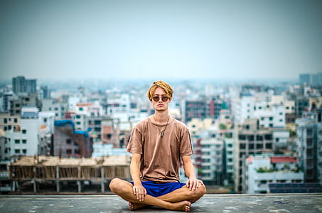 man in brown shirt and blue shorts with yellow turban headdress sitting on the peak of building thumbnail