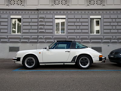 white coupe parked in front of black vehicle beside gray painted building at daytime thumbnail