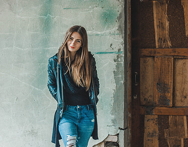 woman wears black zip-up coat with black inner shirt and distressed blue denim jeans thumbnail