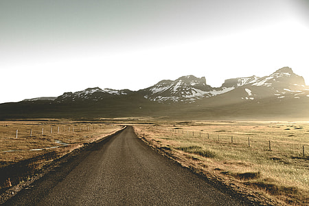 road between field near glacier mountains during day thumbnail