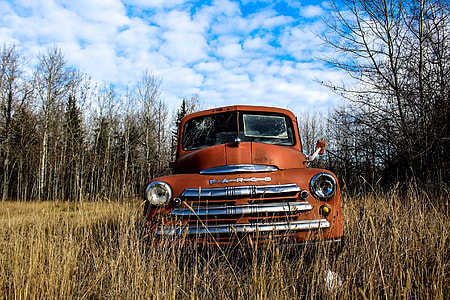 orange classic car on wood under blue sky and white clouds during daytime thumbnail