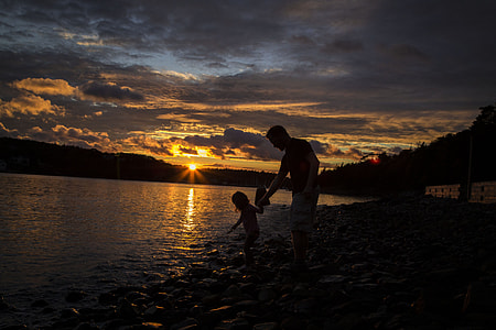 man holding the child on the body of water in golden hour photo thumbnail
