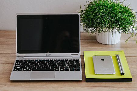 Silver Acer laptop, a white Apple iPhone and a notepad on a wooden desk thumbnail