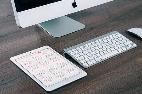white iPad and silver Mac Keyboard on brown wooden surface thumbnail