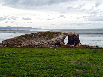 natural arch near green grass field and body of water thumbnail