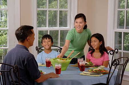 woman standing beside two kids near man sitting on dining table thumbnail