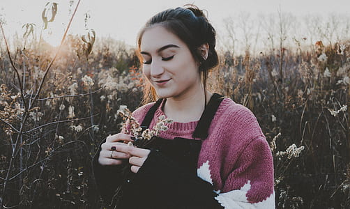 woman in pink sweatshirt holding flower in front of field of grass thumbnail