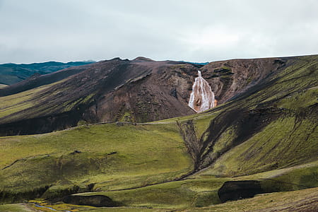 A waterfall surrounded by green hills on a cloudy day thumbnail