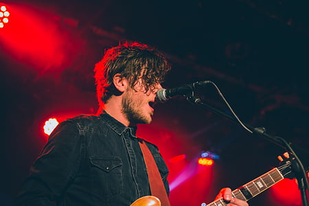 man singing while playing guitar on stage thumbnail