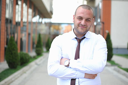 man in white dress shirt with brown silk necktie standing near building thumbnail