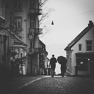 Grayscale Photo Of Man Beside Woman Under Umbrella Walking On Pavement thumbnail