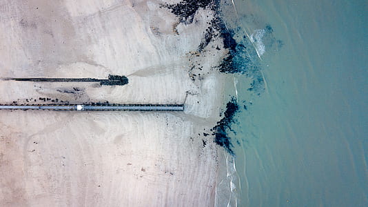 aerial photography of grey pipe on seashore near blue body of water thumbnail