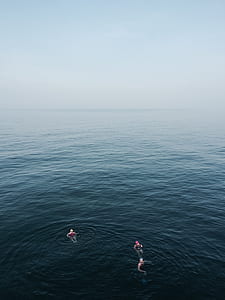 three people swimming on calm body of water thumbnail