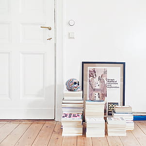 assorted-title books piled beside white door thumbnail
