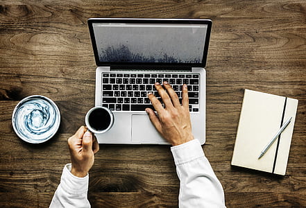 person holding a cup of coffee while using a laptop thumbnail