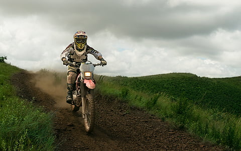 man riding on motocross dirt bike between grasses thumbnail