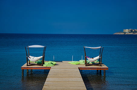 person lying on hammock on brown wooden dock beside calm water duringdaytime thumbnail