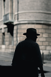 man wearing hat and dress standing in front of a high rise building thumbnail