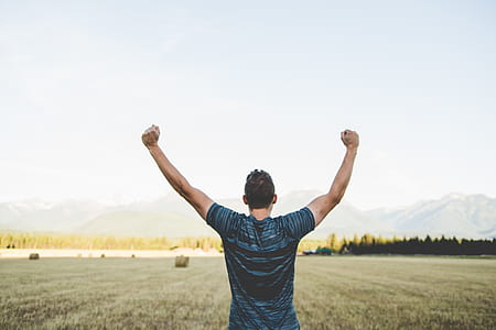 man raising his both hands while standing on green grass field thumbnail
