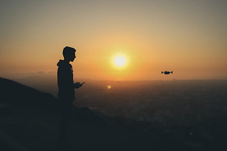 silhouette of person flying drone on mountain in distant of buildings thumbnail