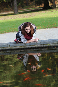woman leaning on the concrete fish pond while holding a red and black camera during daytime thumbnail