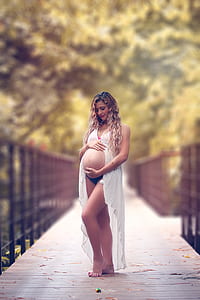 pregnant woman holding her tummy standing on bridge thumbnail