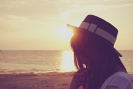 woman in white shirt wearing fedora hat near sea shore during sunset thumbnail