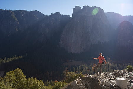 man standing on gray rocks facing green forest thumbnail