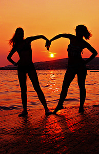 silhouette of woman standing near body of water during sunset thumbnail