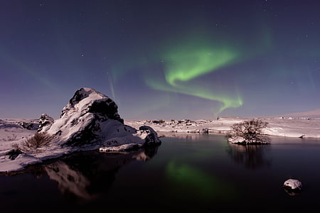 calm body of water facing brown mountain during aurora borealis thumbnail
