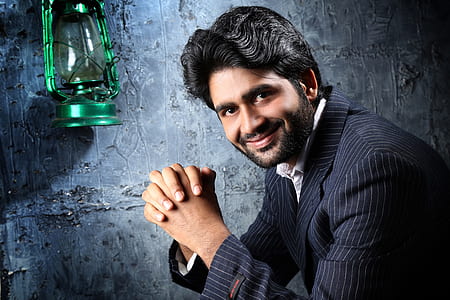 smiling man in black and gray pinstriped blazer beside green lantern hanged on gray wall thumbnail