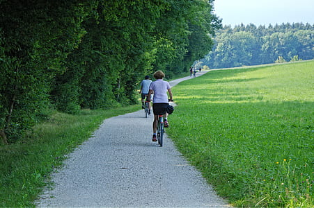 woman riding bicycle on pathway between green grass and trees at daytime thumbnail