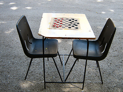 chessboard set on brown wooden table with chairs surrounded by gray soil thumbnail