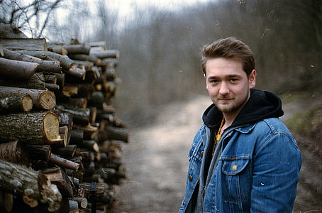 man wearing blue denim hooded jacket beside chopped tree logs during daytime thumbnail