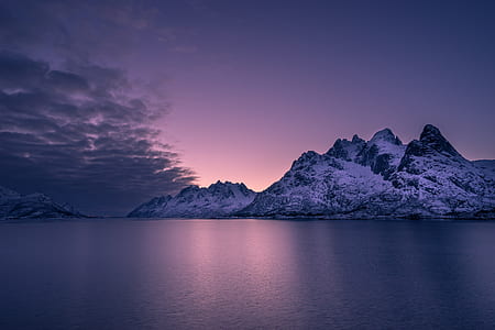 snowy mountain on body of water under cloudy sky thumbnail