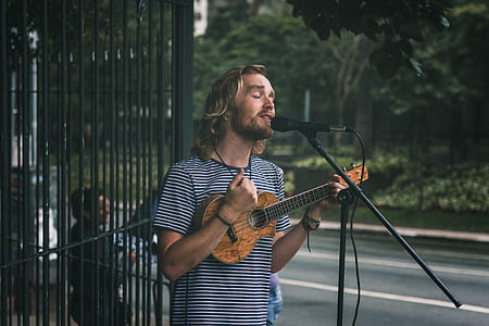 standing man playing ukulele while singing near road thumbnail