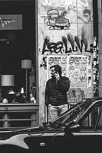 grayscale photography of man standing near shop while having phone conversation thumbnail