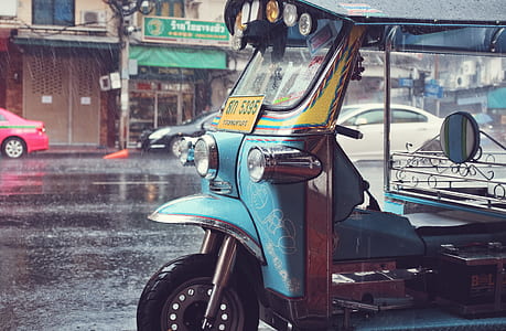 blue auto rickshaw parked on sidewalk while raining thumbnail